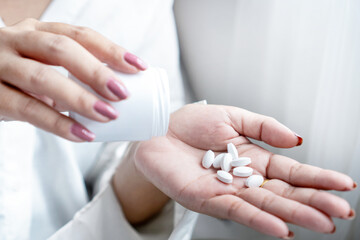 Close-up of a woman’s hand holding a bottle of medicine while taking pills. Concept of overdose...