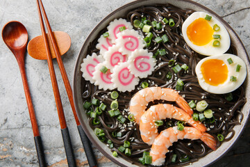 Fish Soba noodles soup with shrimp, narutomaki, green onion and egg close-up in a bowl on the table. Horizontal top view from above
