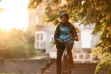 Smiling delivery man riding bicycle at sunset in the city