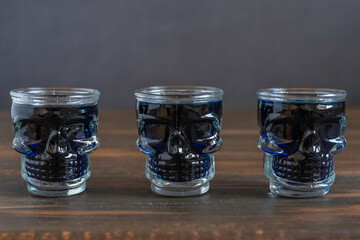 Blue liqueur in skull glasses on dark background. Alcohol drink for Halloween.