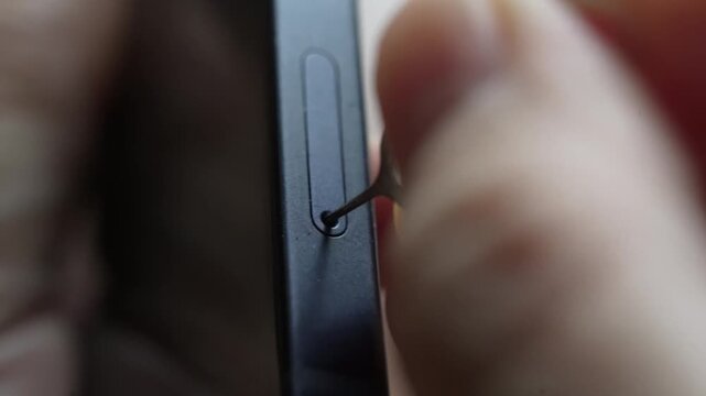 Person taking out and inserting a sim card into back of mobile phone. Sim card in tray being inserted into phone, closeup