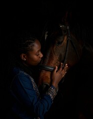 teenage holding head and bonding with bay horse, portrait with black background