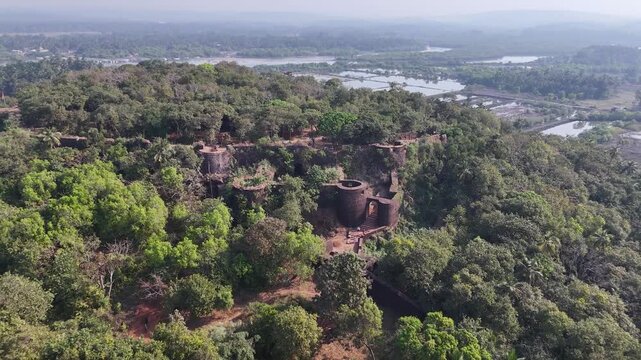 Drone footage reveals the hidden ruins of the historic Redi Fort, reclaimed by a dense tropical forest on a hill in Vengurla, India.