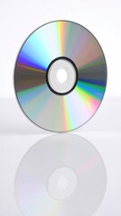 A reflective disc stands, displaying rainbow hues, casting a mirrored image on the glossy surface beneath against a bright, white backdrop