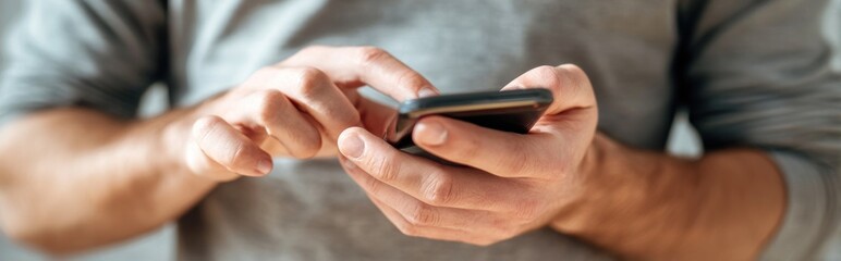 Man using a smartphone with two hands, close-up shot showing fingers tapping the screen, wearing a grey shirt