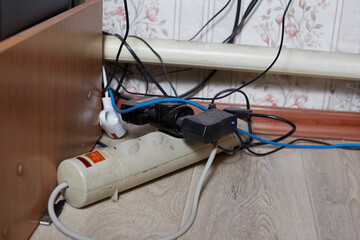 A white power strip with multiple plugged-in devices lies on a wooden floor