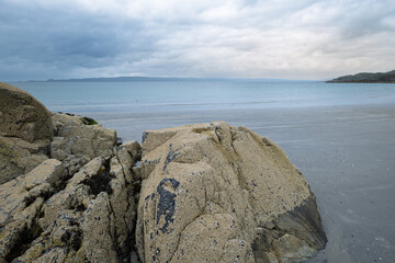 Barnacle encrusted rocks on the shore of a sandy beach along the coastline at Arisaig in the Scottish Highlands