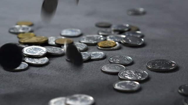 Metal coins fall onto a gray surface and spill in all directions,
Coins raining down from above onto the surface.
Many kopecks fall onto the gray table.
Money, coins, kopecks, pennies