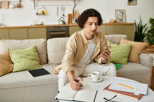 Handsome young man in stylish attire focuses on smartphone while writing notes in peaceful setting
