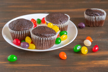 Chocolate muffins and colorful jelly candies for kid's party on dark wooden background.
