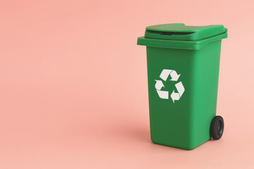 Isolated green recycling bin with black wheels and a white recycle symbol on a coral studio background. Space for text on the side. Clean, commercial image of sustainability