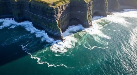High-angle view of dramatic coastal cliffs meeting turquoise waves, showcasing a powerful and serene interplay of land and sea.
