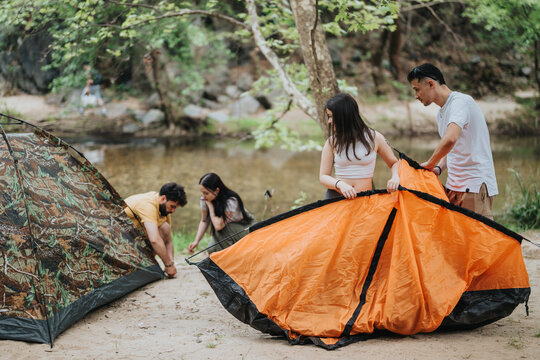 Friends enjoying an outdoor camping trip by a river, assembling tents together amid nature. - Powered by Adobe