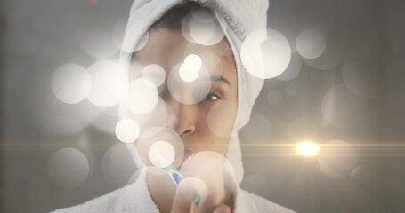 Brushing teeth woman wearing towel and bathrobe in bathroom, with toothbrush bokeh and lens flare