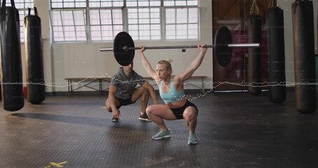 Performing overhead squat with barbell, woman in sportswear at gym with trainer spotting