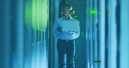 Walking African American engineer with red headphones monitoring racks in datacenter holding laptop
