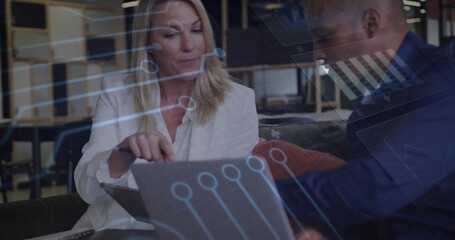 Reviewing data on laptop and tablet on office bench in blazers, colleagues using digital overlays