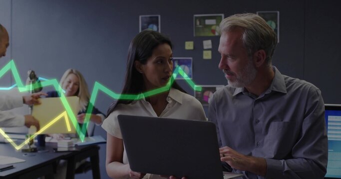 Woman in business attire and man discussing data on laptop at office area, with sticky notes