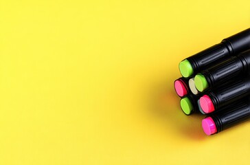 Markers on a yellow background featuring green and pink tip markers, black bodies, and geometric grips