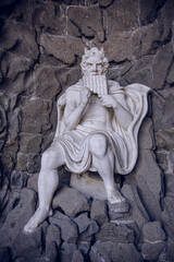 Obraz premium Ancient stone sculpture of mythological figure sitting and playing pan pipes on rocks