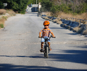 Obraz premium small brave three year old boy in a helmet rides a bicycle on city road by himself