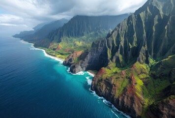 Obraz premium An aerial view captures jagged, lush mountains meeting vibrant turquoise ocean under a cloudy sky. Striking contrast of colors and textures is present