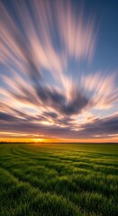 A vibrant sunset paints a field of green grass with streaks of colorful clouds.