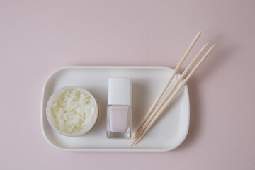 Nail polish and manicure tools, hand cream and wax on a white tray on a pink background