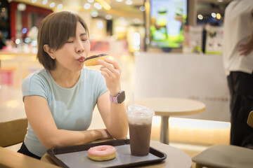 Woman wearing a blue t-shirt is eating a donut while sitting at a donut shop