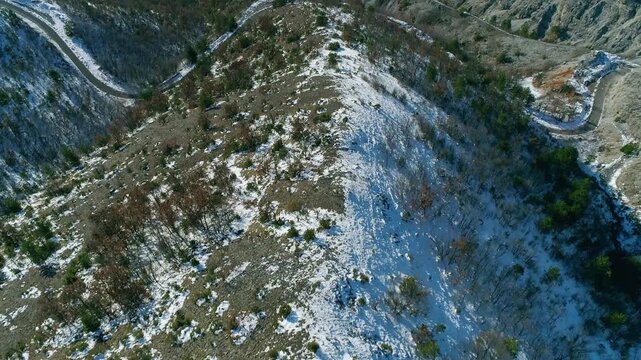 Drone flight over mountain ridge, curvy road across dramatic hills, lake