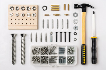 Fototapeta premium collection of hardware tools and components, including screws, nuts, bolts, washers, a hammer, a screwdriver, and a wooden board with pre-drilled holes.