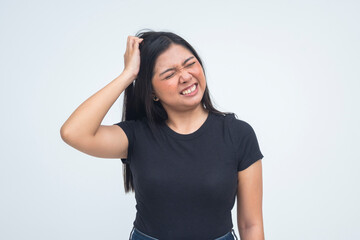 A helpless young Asian woman in a half body shot scratching her head intensely with a grimace that...