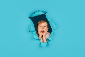 Surprised boy looking through hole in paper wall. Spy child watching through hole. Breaking paper...