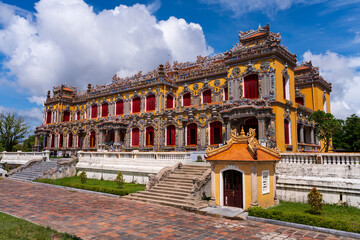 The magnificent, recently restored Kien Trung Palace in Hue, showcasing a vibrant yellow facade, striking red windows, and highly intricate architectural details under a cloudy sky.