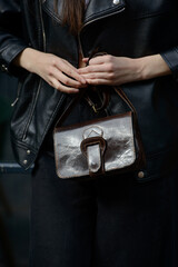 A stylish model in a black leather jacket showcases a unique black leather cross-body bag with a glossy sheen and a front flap pocket