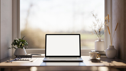 Fototapeta premium Blank screen laptop with calculator and coffee cup on wooden table under window in warm sunlight.