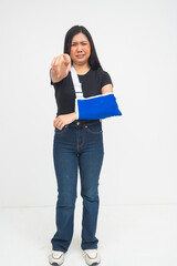 A crying young Asian woman in a full body shot standing with an arm sling while pointing to the camera with her other hand in a blaming manner. Isolated on a white background.