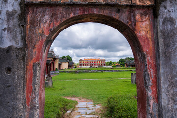 A vibrant, traditional palace in Hue is framed by a weathered, red arched gateway, overlooking a...
