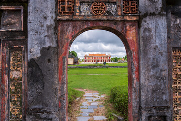 A vibrant, traditional palace in Hue is framed by a weathered, red arched gateway, overlooking a...