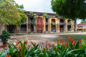 A decaying colonial-era building in Hue's Citadel features a colorful geometric installation, viewed over bright orange flowers and a wet, empty courtyard.