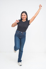 An enthusiastic young Asian woman in a full body shot almost jumping with one foot up, fist raised, and smiling excitedly. Isolated on a white background.