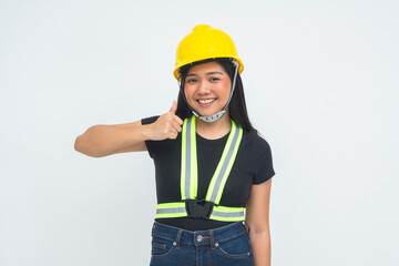 A positive young female engineer in a half body shot smiling brightly, giving a thumbs up while wearing a protective helmet, conveying approval. Isolated on a white background.