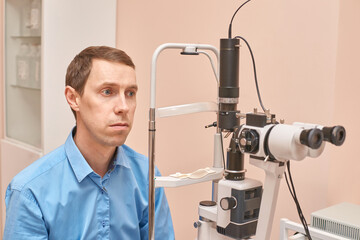 Caucasian male adult undergoing eye exam with slit lamp in ophthalmology clinic.