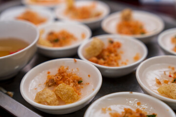 Tiny white bowls hold Beo cake  from Hue, topped with savory ground shrimp and crispy pork rinds, with a small bowl of dipping sauce visible.