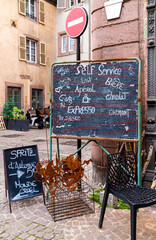 Rustic sign indicating dining options in a narrow French old town, showing the offerings of nearby cafés.