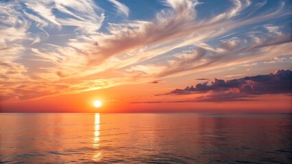 Obraz premium Vibrant sunset over calm ocean waters with wispy clouds