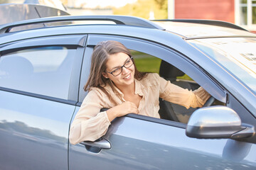 Young caucasian female driver smiling in car window with glasses in bright daytime scene.