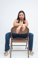 A fierce young Asian woman sitting on a backward chair with a strong, intense gaze that exudes confidence and power. Isolated on a white background.
