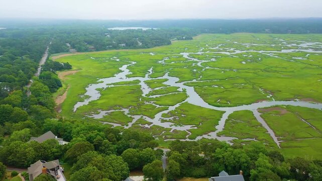 High-resolution aerial footage of Cape Cod&rsquo;s coastal marshes, showing tidal waterways, mudflats, and lush green grasses blending naturally into wooded neighborhoods.