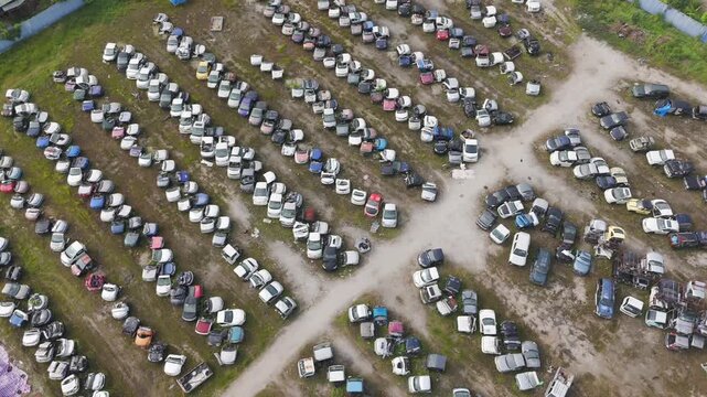 A detailed aerial view of a sprawling car scrapyard and spare parts facility, showcasing thousands of dismantled vehicles, engine blocks, body shells, hoods, and used parts arranged in organised rows.